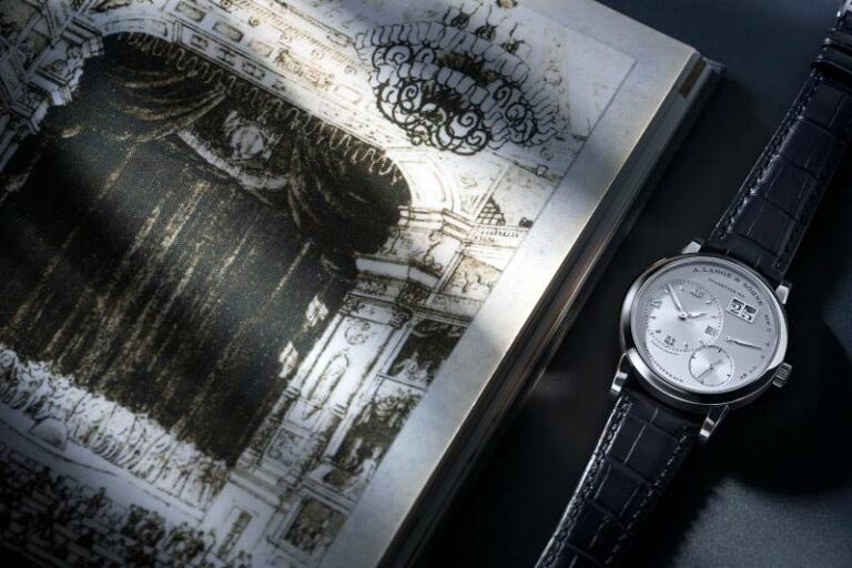 Lange 1 In White Gold Next to A Drawing of The Royal Court Theatre